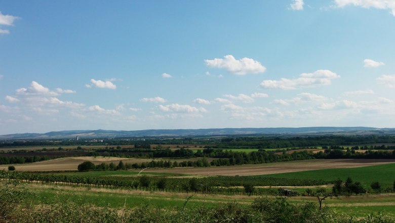 Wide landscape with fields and hills under a blue sky with clouds.