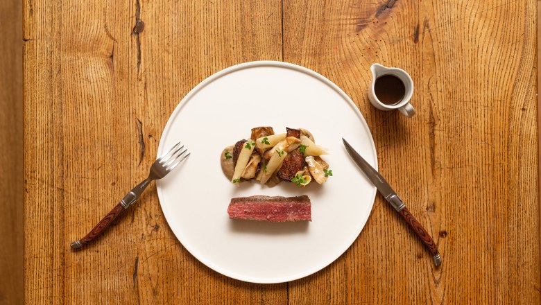 A plate of venison, artichokes, king oyster mushrooms and Jerusalem artichokes on a wooden table.
