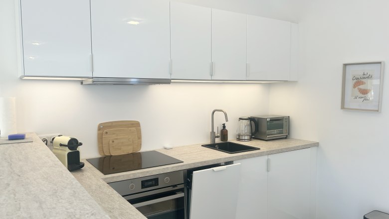 Modern kitchen with white cupboards, stove, sink and coffee machine.