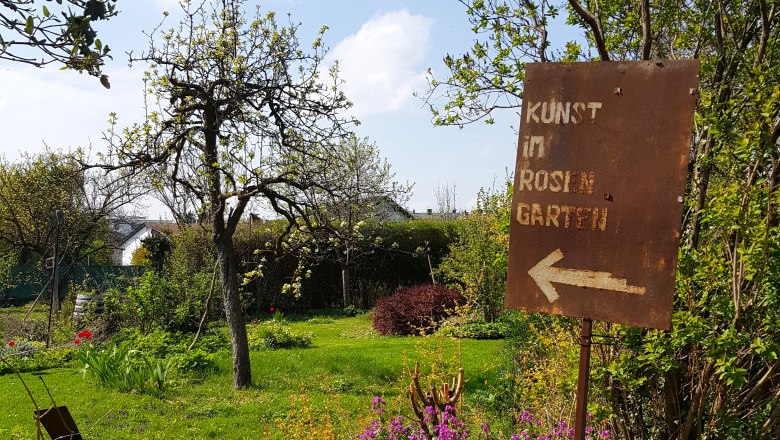 A garden with a sign pointing to the art in the rose garden.