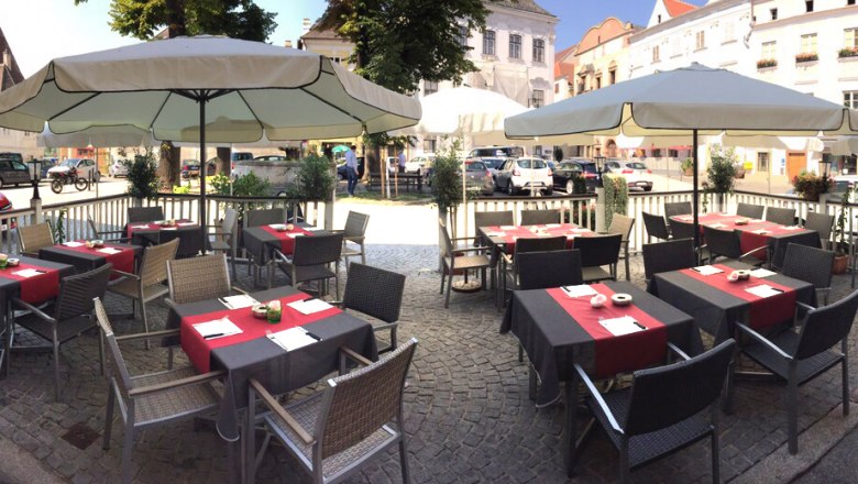 Outdoor terrace of a café with tables and parasols on a paved square.