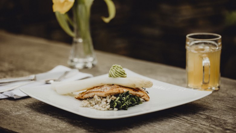 Gourmet dish with asparagus, fish and vegetables on a wooden table, yellow flower in the background.