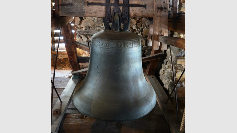 Large bell in a wooden belfry, surrounded by stone walls.