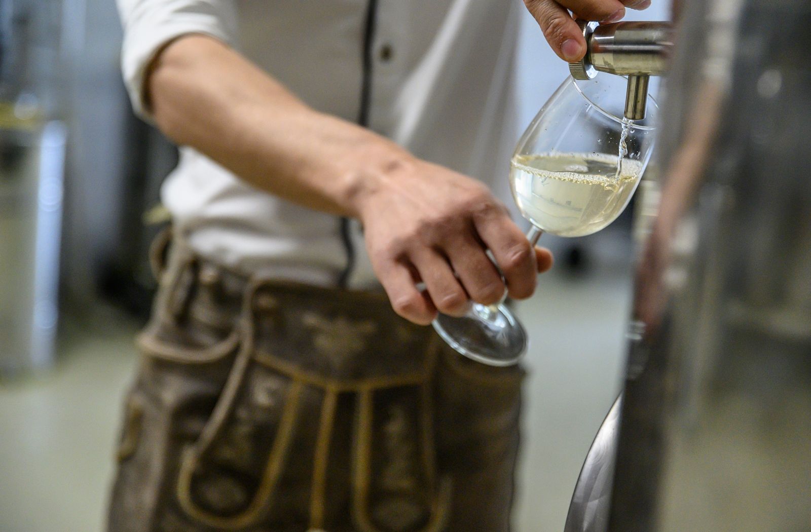 Person fills a glass with white drink from a stainless steel container.