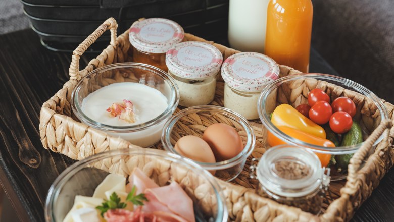 Breakfast tray with bread rolls, croissant, milk, juice, yogurt, eggs, cold cuts and vegetables.