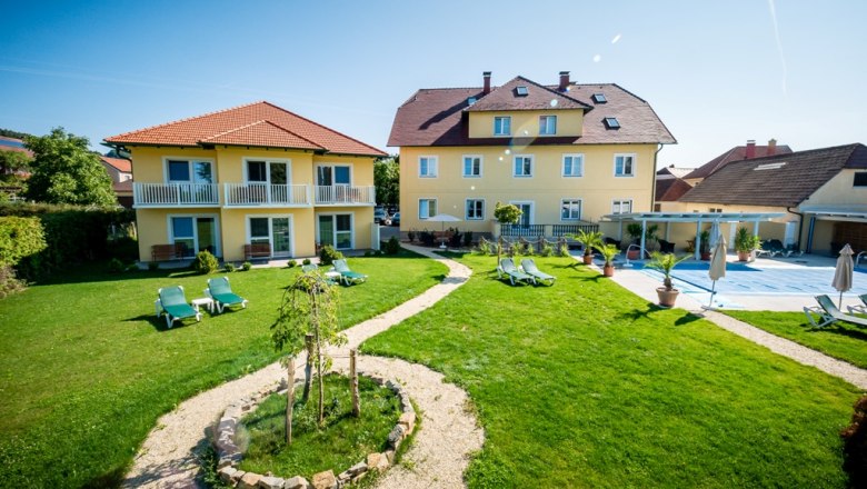 Garden area with yellow buildings and sun loungers in sunny weather.