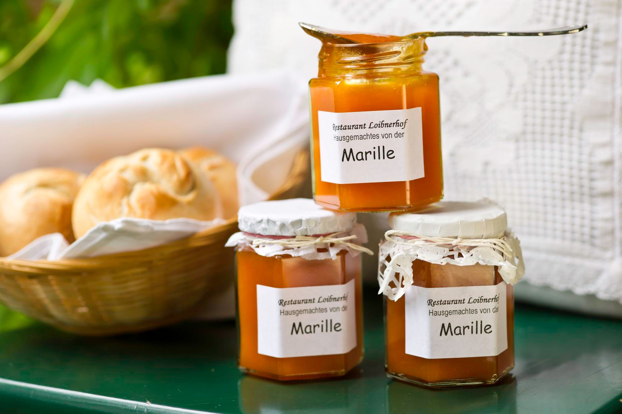 Three jars of apricot jam from the Loibnerhof restaurant next to a basket of bread rolls.