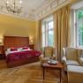 Elegant double room with large bed, two armchairs, table and large windows with a view of the greenery.