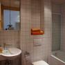 Modern bathroom with white tiles, washbasin, toilet and bathtub. Towels on a shelf.