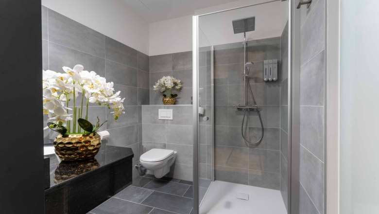 Modern bathroom with gray tiles, shower, toilet and orchids in golden vases.