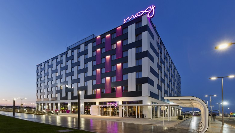 moxy-vienna-airport_hotel, © MOXY Vienna Airport Exterior view of the Moxy Vienna Airport Hotel at dusk with illuminated lettering.