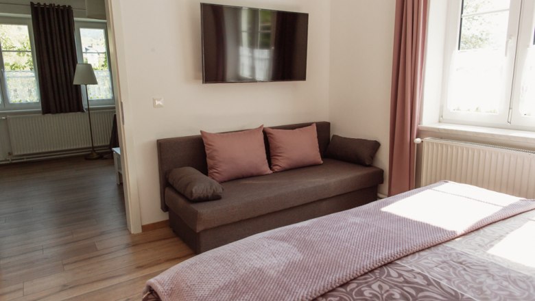 Modern living room with sofa, flat screen TV and window with pink curtains.