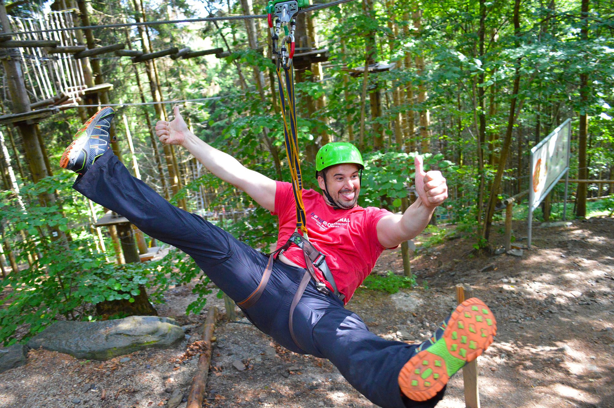 Person wearing a helmet and safety harness on a zip line in the forest.