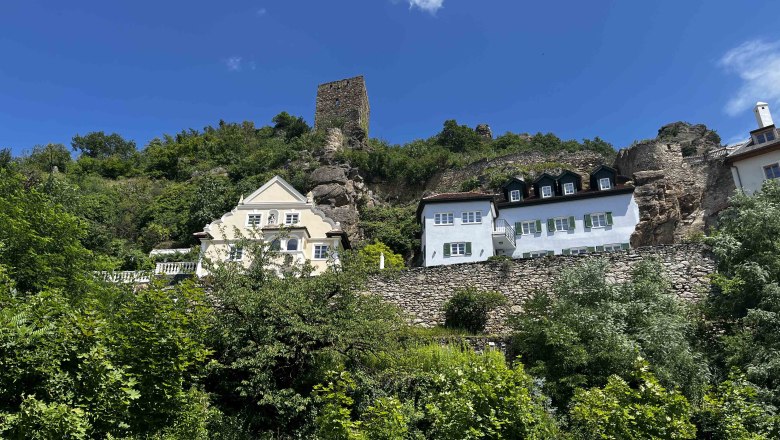 View of D&uuml;rnstein with historic buildings and ruins on a hill, surrounded by green vegetation and blue sky.