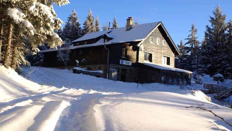 Winter impression - Herrgottschnitzerhütte, © Herrgottschnitzer-Franz-Kaupe-Haus, Mimm Snow-covered hut in the forest in the sunshine.