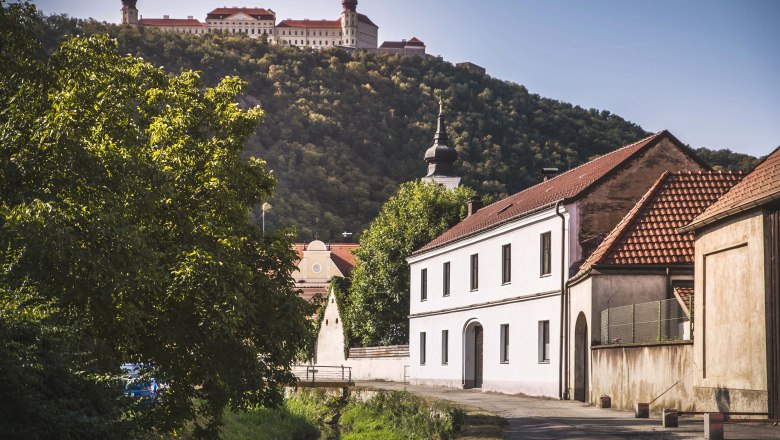 View of Göttweig Abbey on a hill, surrounded by trees, with buildings in the foreground.