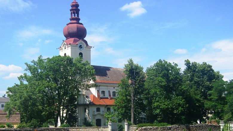 Baroque church with red tower and garden in the foreground.