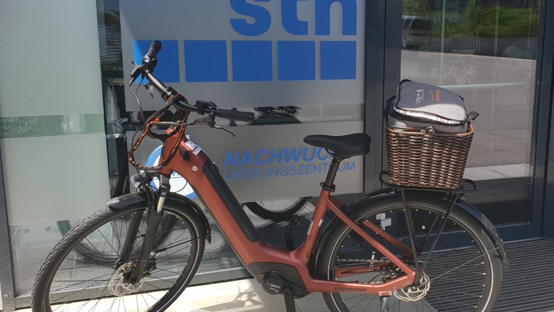 A red e-bike stands in front of a building with the inscription 'sth Nachwuchsleistungszentrum'.
