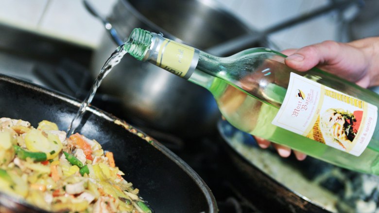 A hand pours Cider from a bottle into a pan of vegetables.