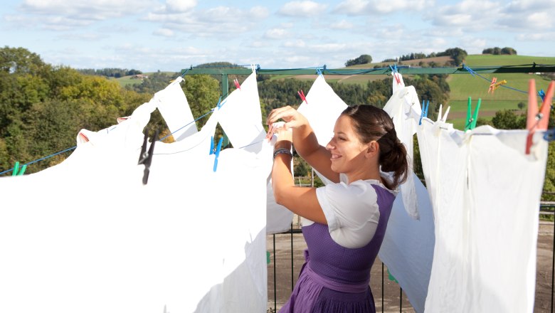 Woman hangs laundry outdoors, with rural landscape in the background.