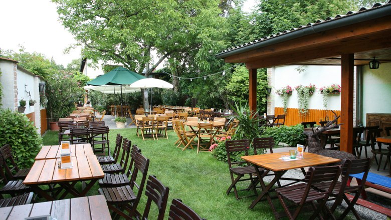 A cozy beer garden with wooden tables and chairs, surrounded by green trees and plants.