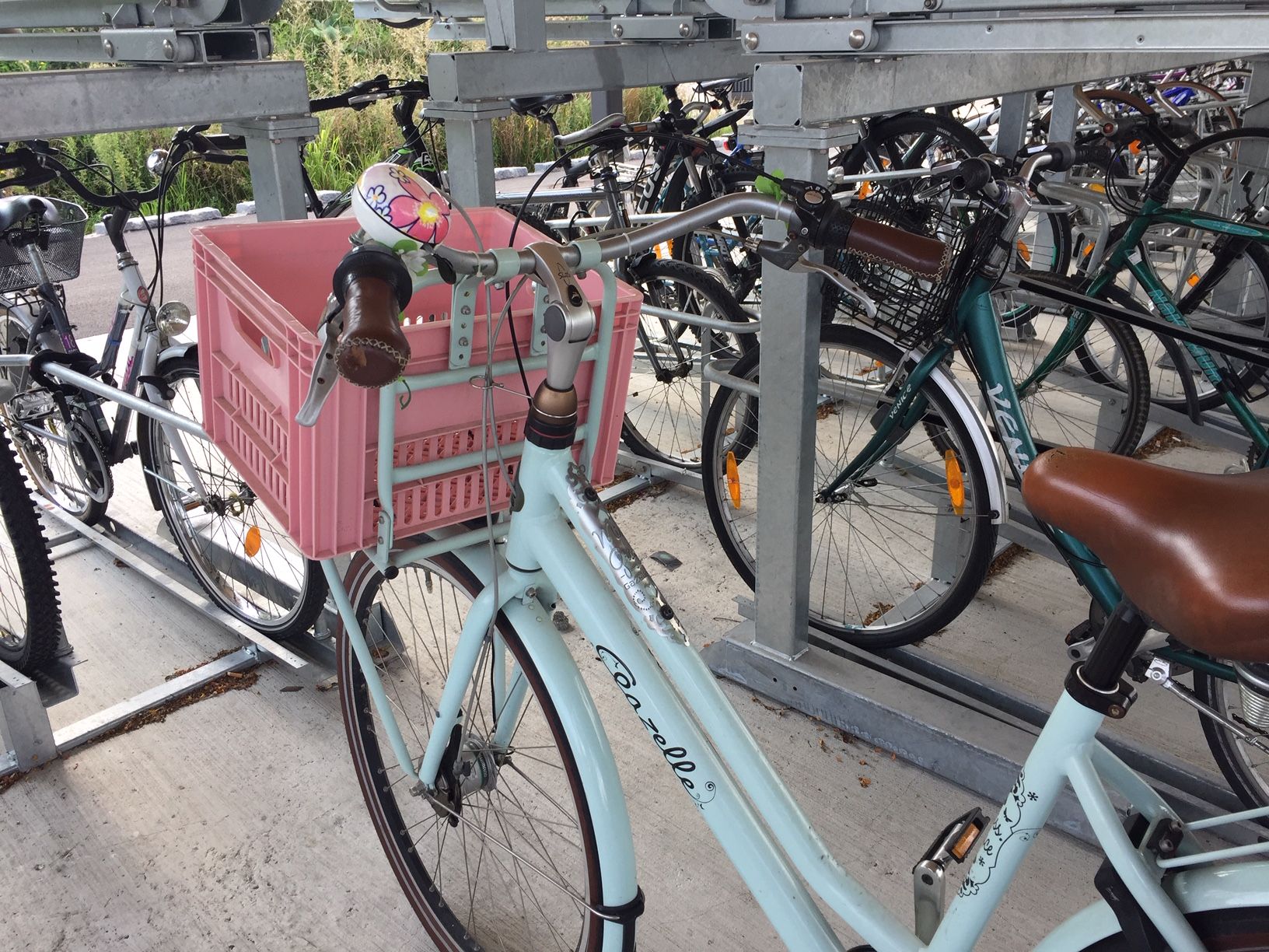 Bicycle with pink crate in a bicycle stand.