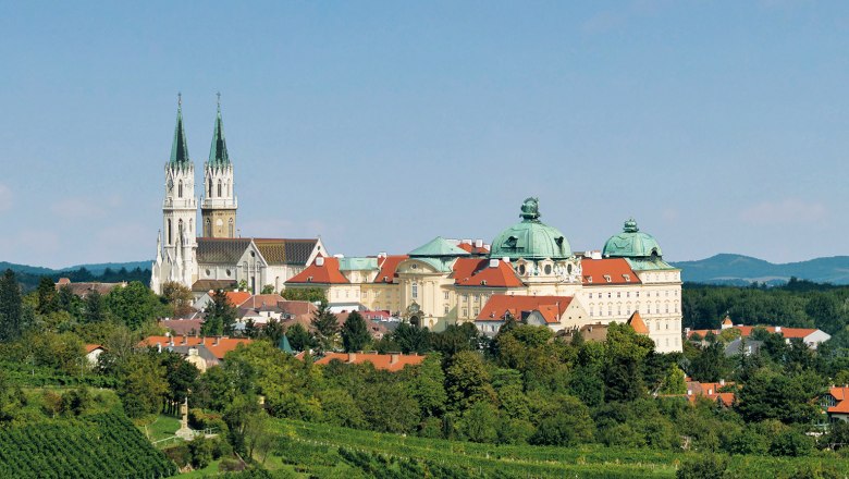 Panoramic view of Stift Klosterneuburg with green vineyards in the foreground.