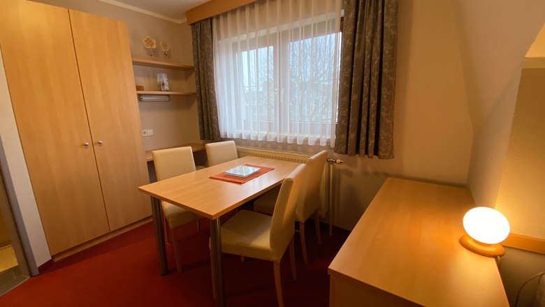 A cozy room with wooden furniture, table, chairs and a window with curtains.