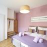 A cozy guest room with a pink wall, double bed and modern furnishings.