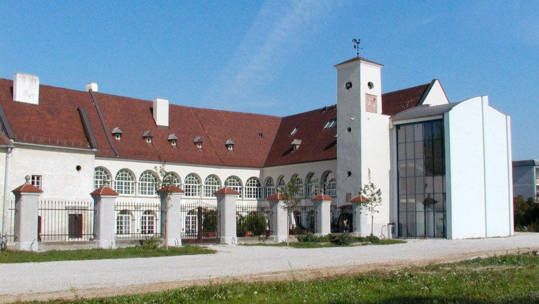 Katzelsdorf Castle with modern extension and historic building. White fa&ccedil;ade with rounded windows, red roof and large inner courtyard