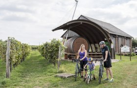 A family with bicycles in front of a winery with a large barrel in Hohenruppersdorf.