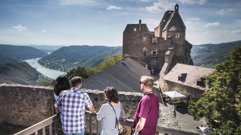 People in a castle with a view of the river and mountains.