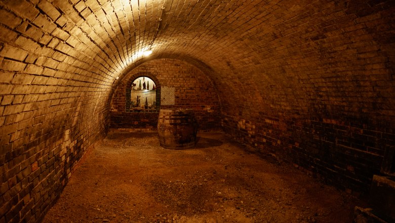 A vaulted brick cellar with a barrel and an illuminated shelf in the background.