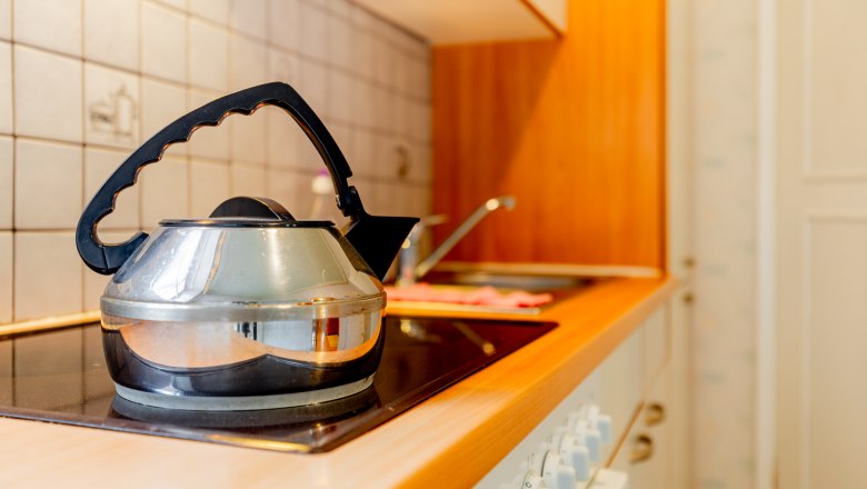 A kettle stands on a stove in a kitchen with wooden elements and tiles.
