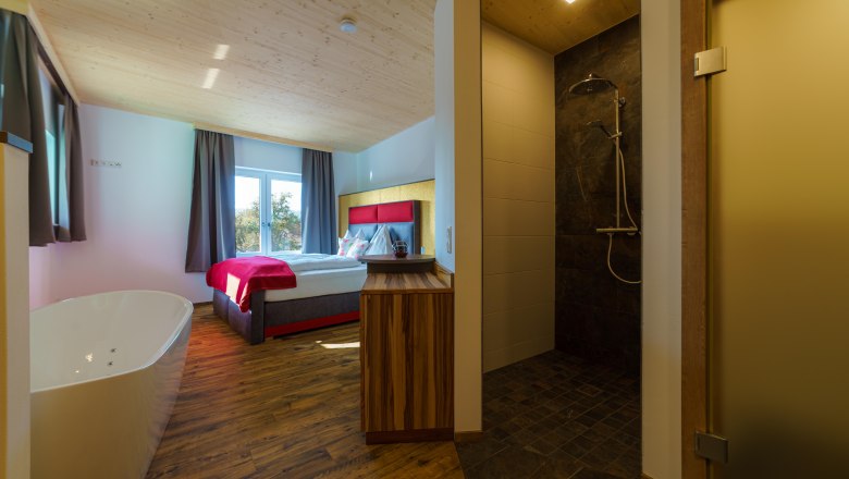 A cozy room with double bed, free-standing bathtub and modern shower.
