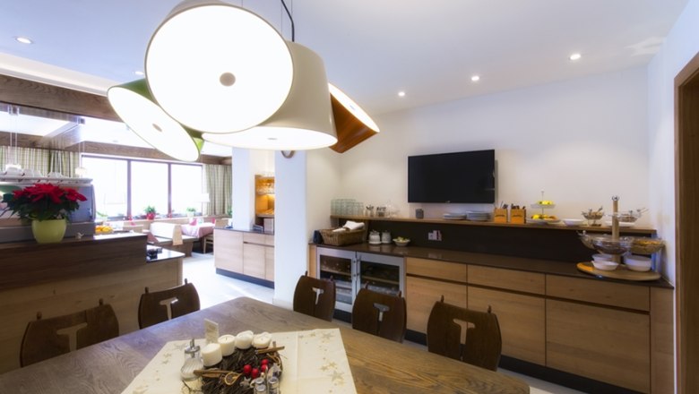 A modern restaurant with wooden furniture, a large table, decorative lamps and a TV on the wall.