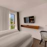 Modern hotel room with large bed, flat screen TV, desk and chair. Window with view of trees.