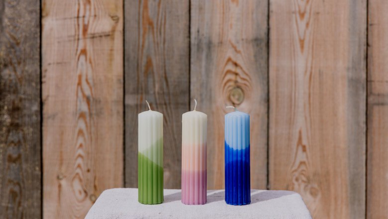 Three colorful candles on a table in front of a wooden wall.