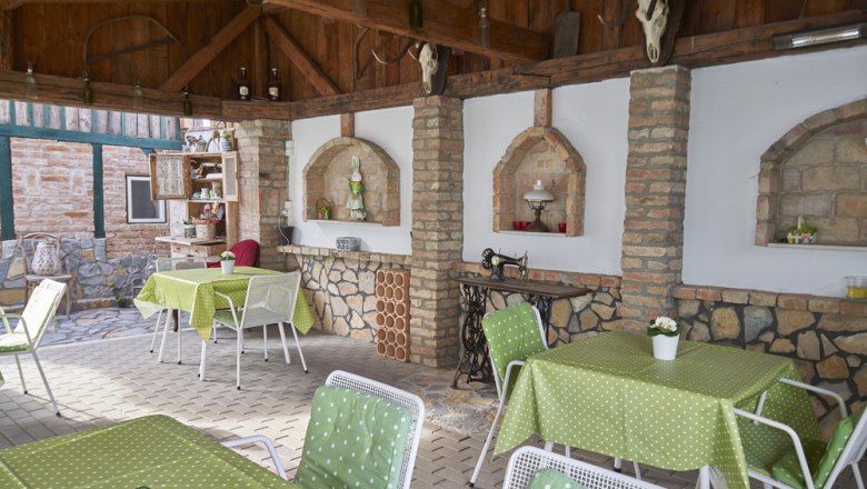 Covered terrace with green tablecloths, white chairs and rustic decorations.