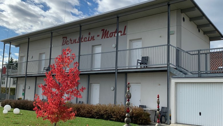 Two-story building with the inscription 'Bernstein Motel', red tree in the foreground, blue sky with clouds.