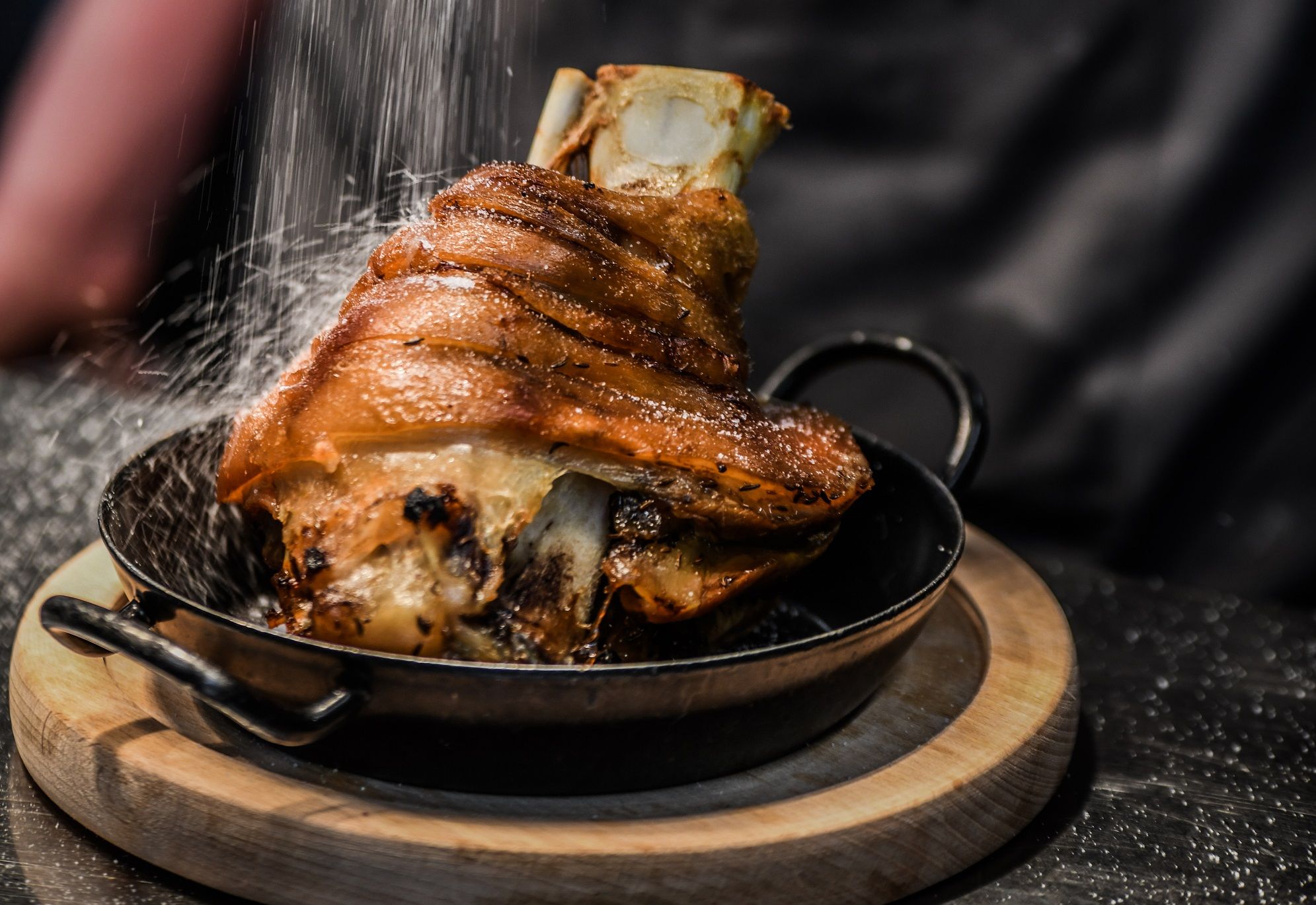 Crispy pork knuckle in a pan on a wooden board, sprinkled with salt.