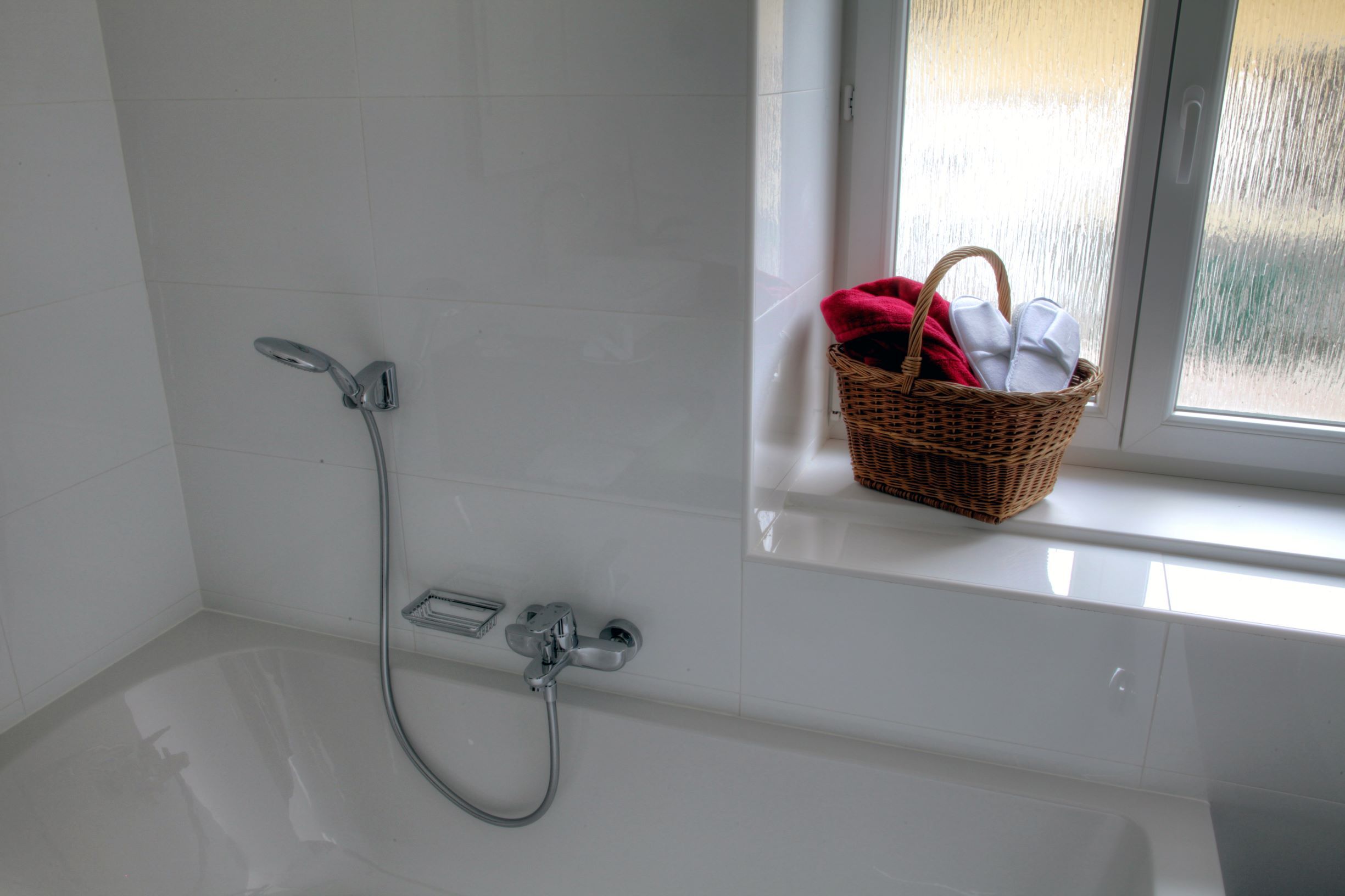 White bathtub with shower head, next to it a window sill with a basket full of towels.