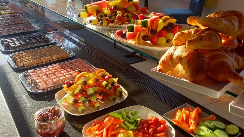 A buffet with croissants, fruit skewers, vegetables and olives in a sun-drenched room.