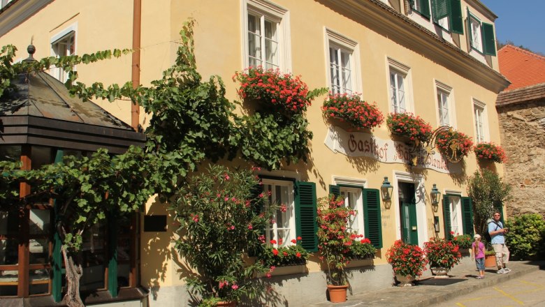 Hotel, © Schendl A traditional inn with a yellow façade, green shutters and flower boxes in bloom.