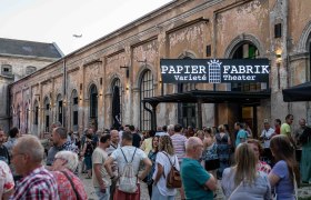 Crowd in front of an old paper factory with a sign 'Papier Fabrik Variet&eacute; Theater'.