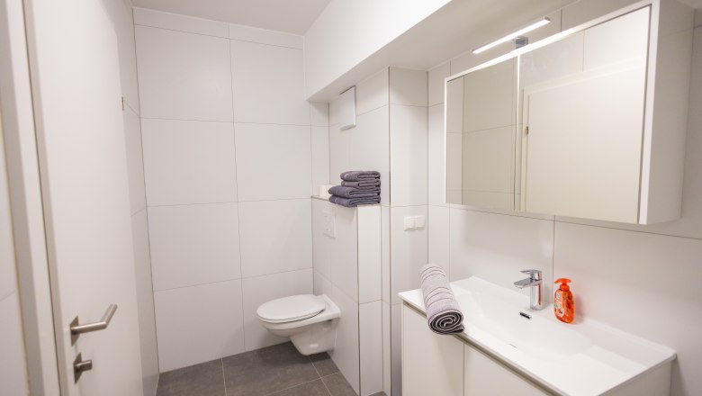 Modern bathroom with white tiles, washbasin, mirror and toilet.