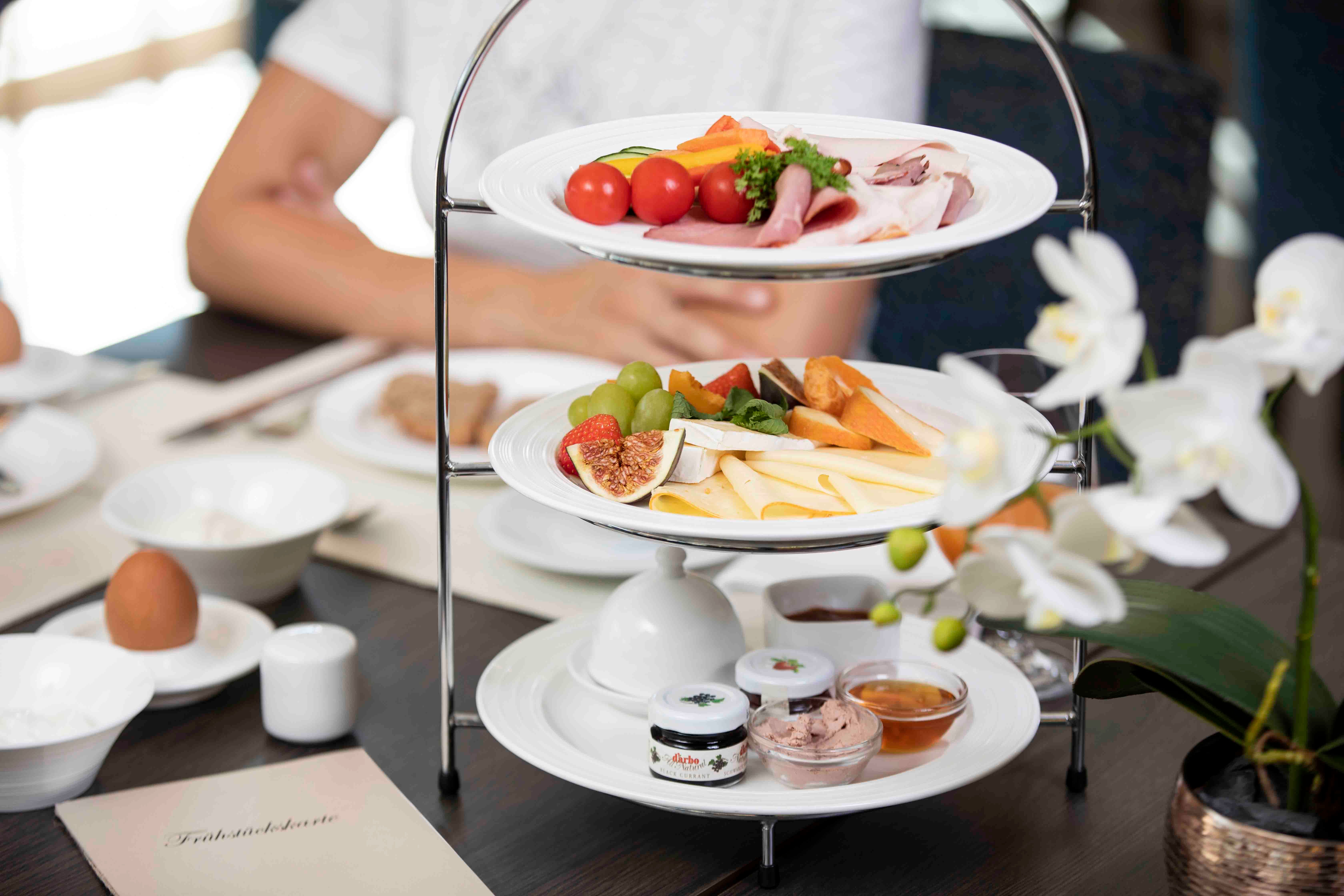 A breakfast table with an etagere full of cheese, cold cuts, fruit and spreads. A white orchid in the foreground.