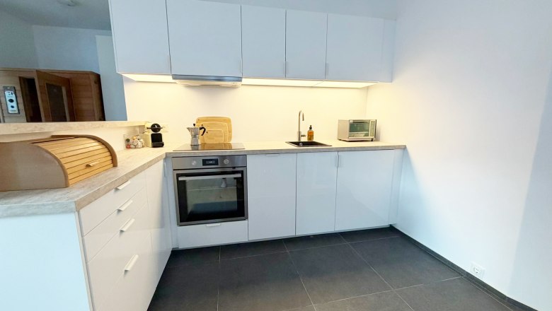Modern kitchen with white cupboards, oven, sink and toaster.