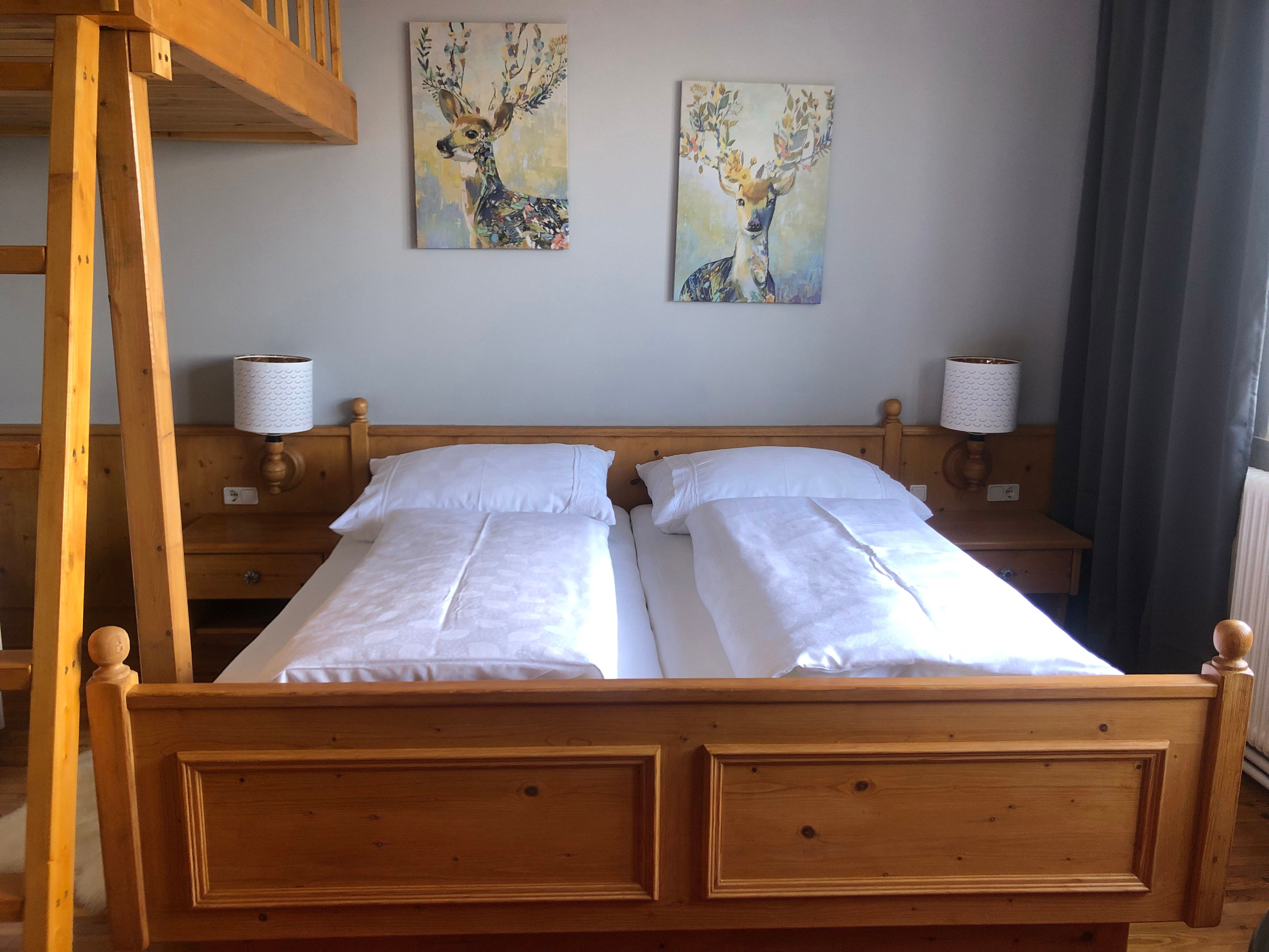 Cozy bedroom with wooden furniture, double bed, two deer paintings on the wall and a ladder to a loft bed.
