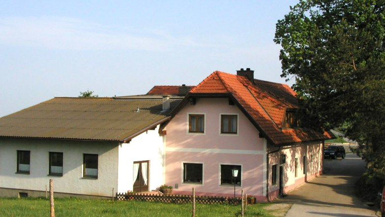 A traditional inn with pink and white walls and a red tiled roof, surrounded by green countryside.